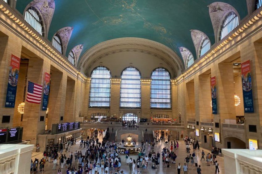 A large indoor space with high ceilings, large arched windows, and numerous people. 4