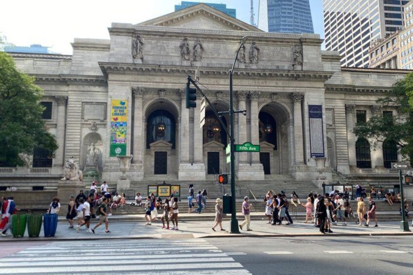 A large public building with classical architecture, a crosswalk, and people walking. 3