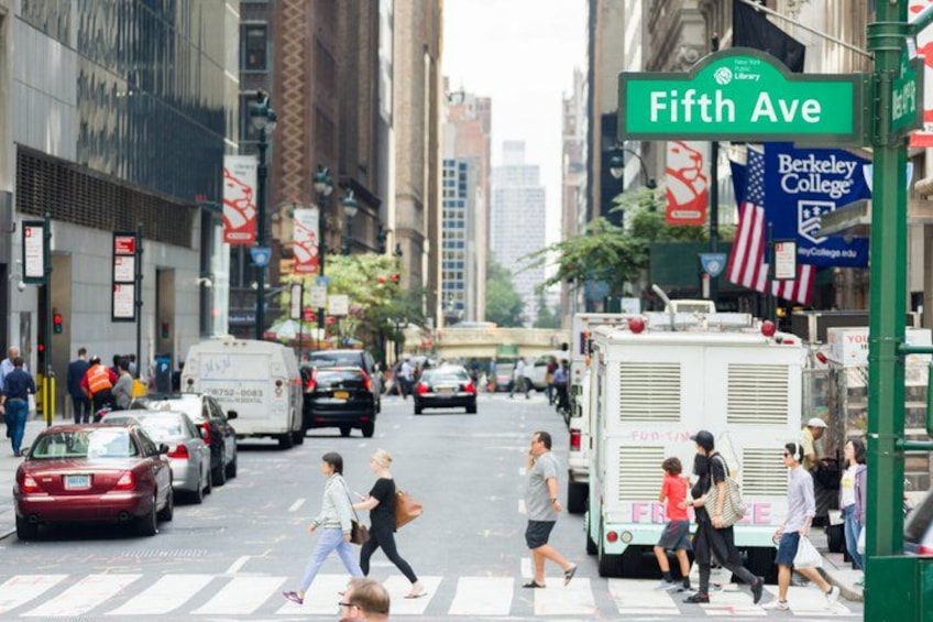 A busy urban street with pedestrians crossing, cars, and a library sign. 2