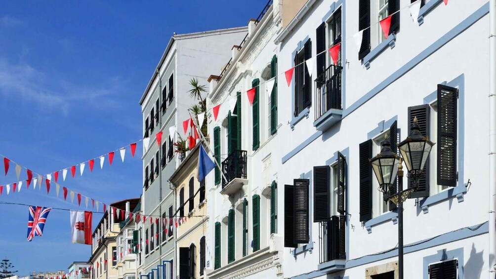 Una calle flanqueada por edificios blancos, banderas rojas y blancas, y un cielo azul despejado. 2