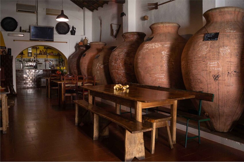 A rustic interior with large clay pots, wooden furniture, and a brick wall. 3