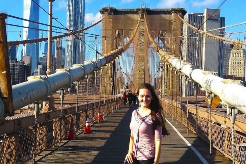 A pedestrian bridge with metal cables and a cityscape in the background. 1