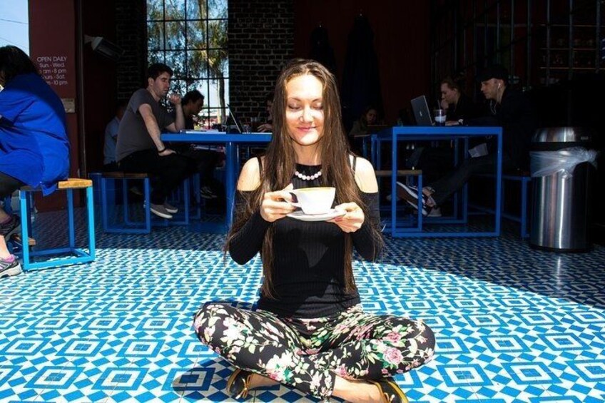 A person sitting on a patterned floor, holding a cup. 3