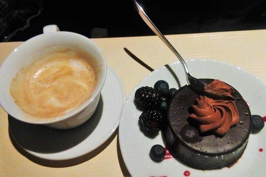 A cup of coffee with a latte art design, a chocolate dessert with whipped cream and berries, and a spoon. 4