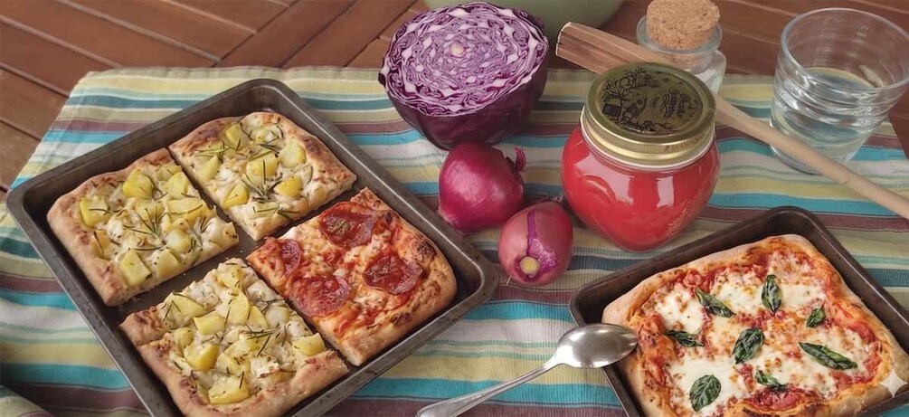 Cuatro pizzas sobre una bandeja, un repollo rojo cortado por la mitad, un frasco de salsa y una cuchara sobre un paño a rayas. 3