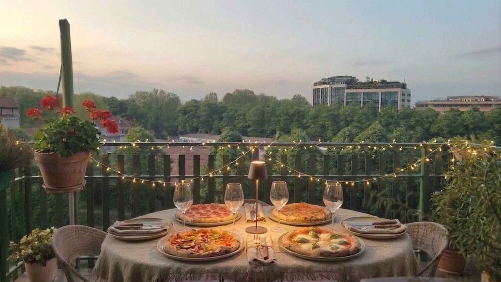 Mesa al aire libre con luces colgantes, platos de pizza y vista a un paisaje urbano de fondo. 1