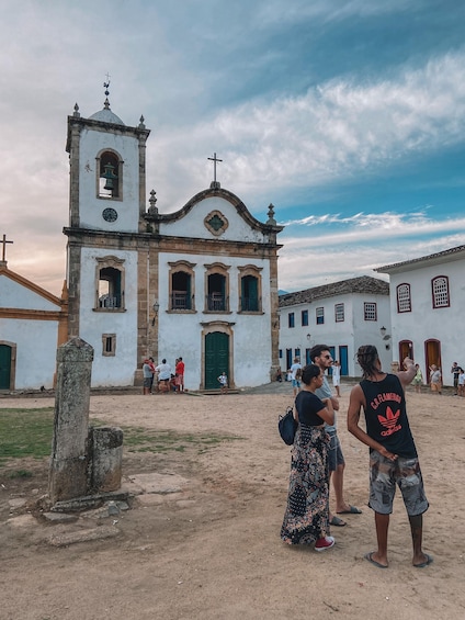 Una iglesia histórica con un campanario, rodeada de gente y suelo arenoso. 1