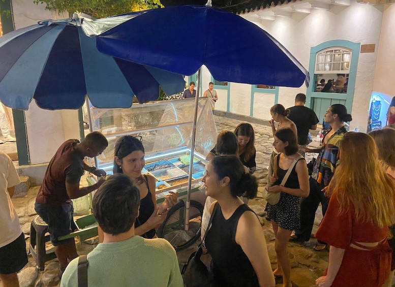 Un grupo de personas reunidas alrededor de una mesa con comida bajo un paraguas azul. 5