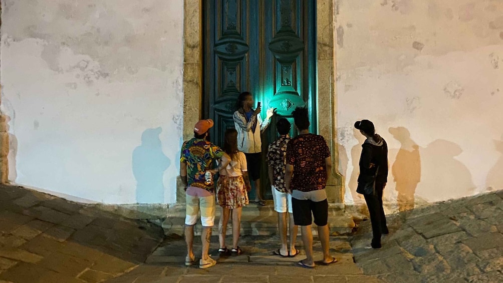 Un grupo de personas de pie frente a un edificio con puerta azul e iluminación verde. 4