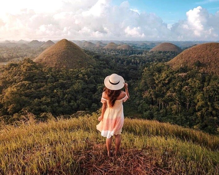A person standing on a grassy hill overlooking a landscape with multiple hills. 1
