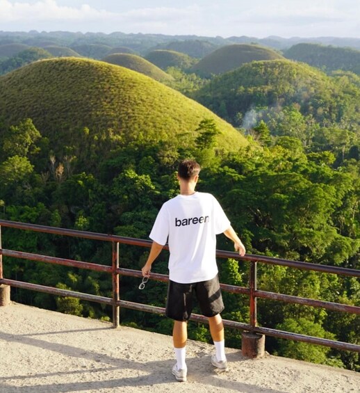 A person standing on a viewing platform overlooking a forested valley with rolling hills. 5