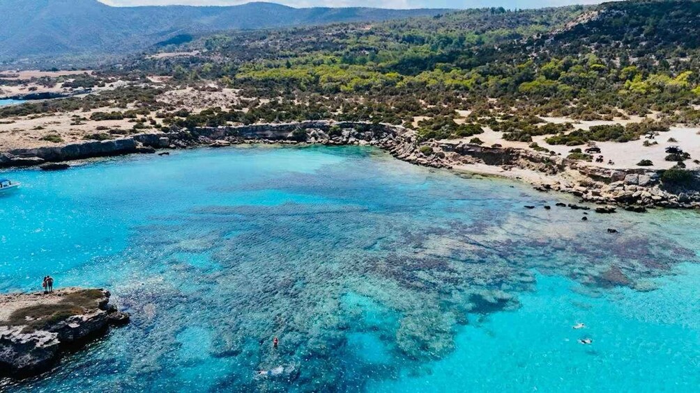 A coastal landscape with clear turquoise waters, rocky shores, and a mountainous backdrop. 3