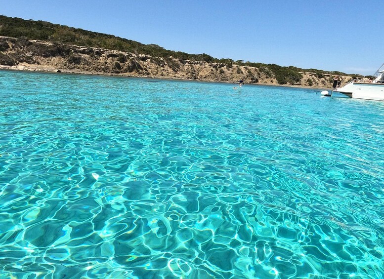 A clear blue sea with a boat and rocky coastline. 4