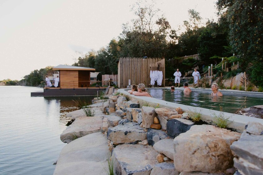 A natural hot spring with people relaxing, surrounded by rocks and trees. 1