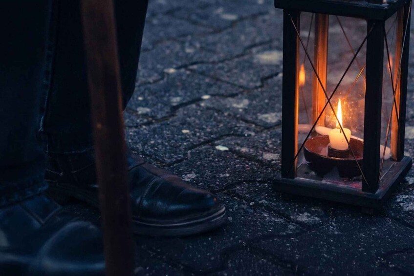 A person's foot next to a lit lantern on a cobblestone surface. 3