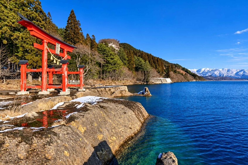 A red torii gate, a rocky shoreline, and a mountain range in the background. 3