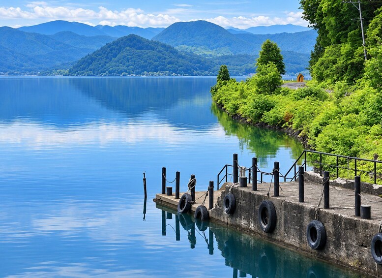 A calm lake with a dock, surrounded by lush greenery and mountains in the background. 5