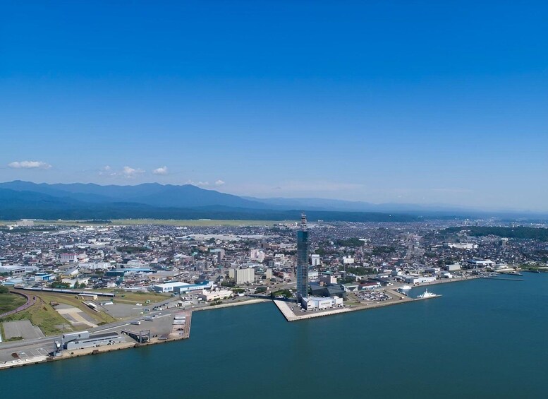 A coastal cityscape with a prominent skyscraper, a marina, and mountains in the background. 4