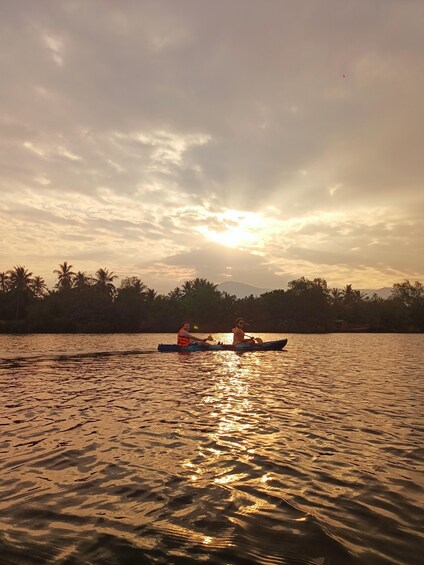 Two people in a kayak on a body of water with a sunset in the background. 5