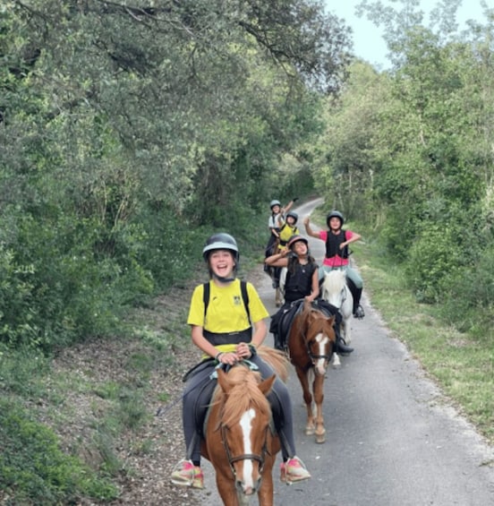 A group of people riding horses on a narrow road surrounded by dense greenery. 3