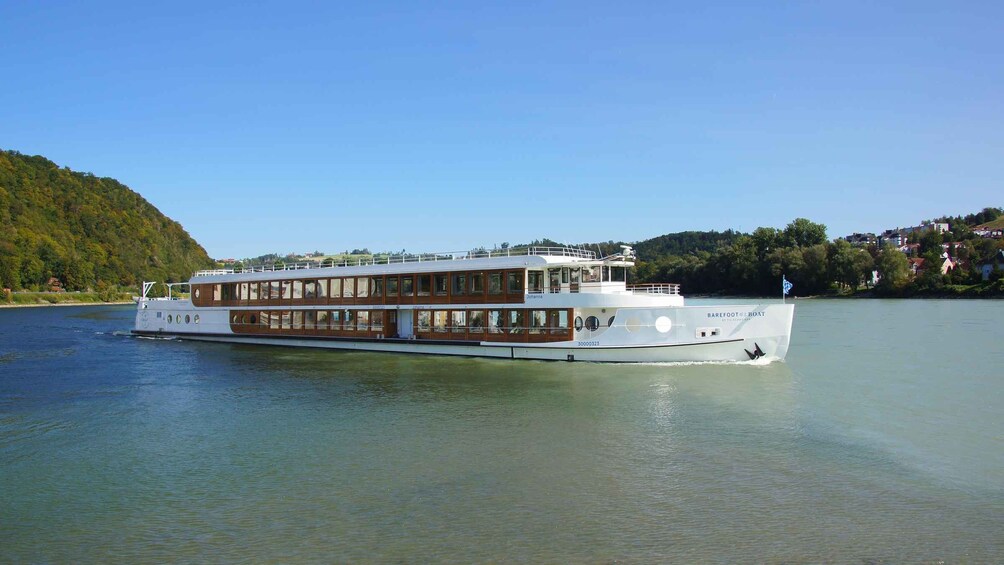 A large riverboat with multiple decks, white hull, and a blue flag on the stern. 1