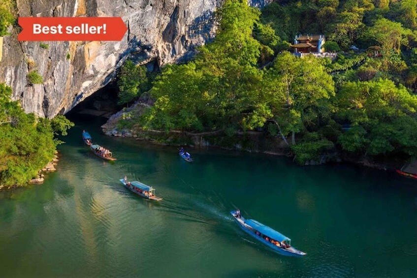 Un río con barcos, la entrada de una cueva y un edificio tradicional rodeado de árboles. 1