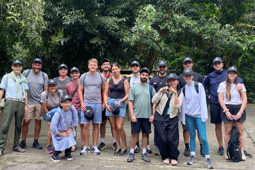 Un grupo de personas al aire libre, algunas con sombreros, de pie sobre un camino de concreto rodeado de follaje. 3