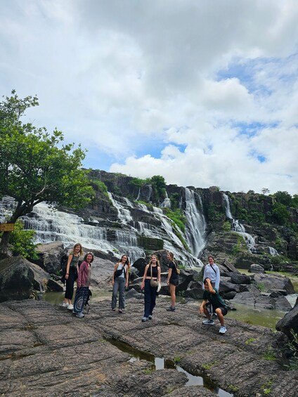 A group of people standing on rocky terrain with a waterfall in the background. 2