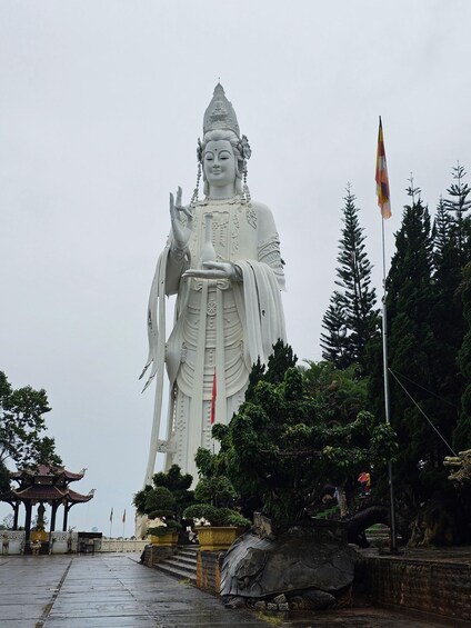 A large white statue of a deity with intricate details, set in a park with trees and a pavilion. 4