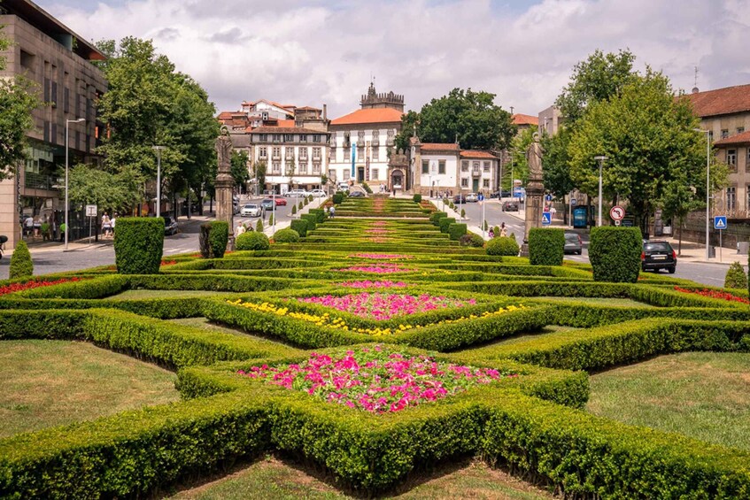 Un jardín formal con setos geométricamente recortados y coloridos macizos de flores, que conduce a un edificio histórico con tejado de tejas rojas. 2