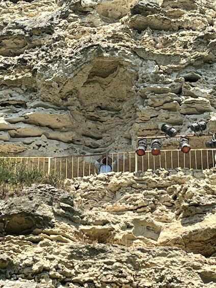 A rocky terrain with a person standing behind a metal fence. 4
