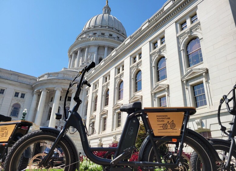 A bicycle with a 'Madison Adventure Tours' sign in front of a large white building with columns and a dome. 1