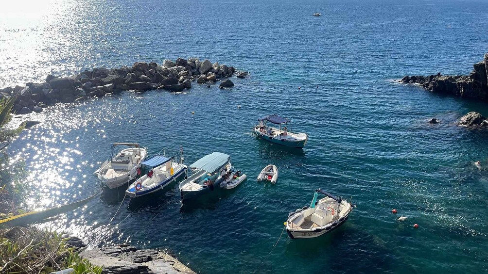 A group of boats docked near a rocky shoreline with clear blue water. 5