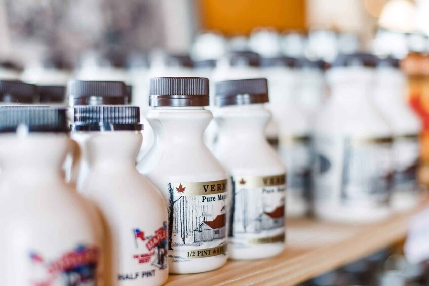 A row of white bottles with labels, some with a maple leaf design, on a wooden shelf. 4