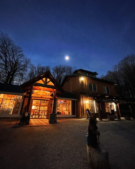 A wooden building with a lit entrance at night, a visible moon in the sky, and bare trees in the background. 1