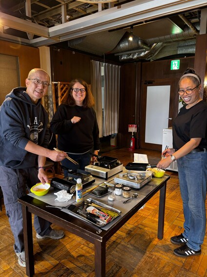 Three people cooking at a table with various kitchen utensils and ingredients. 2