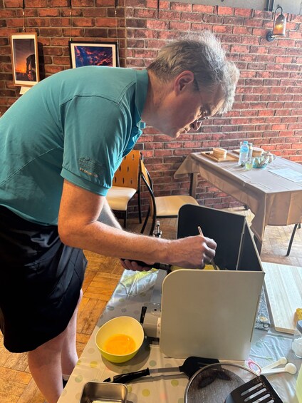 A person in a teal shirt and black shorts preparing food at a table with a laptop, a yellow bowl, and kitchen utensils. 4