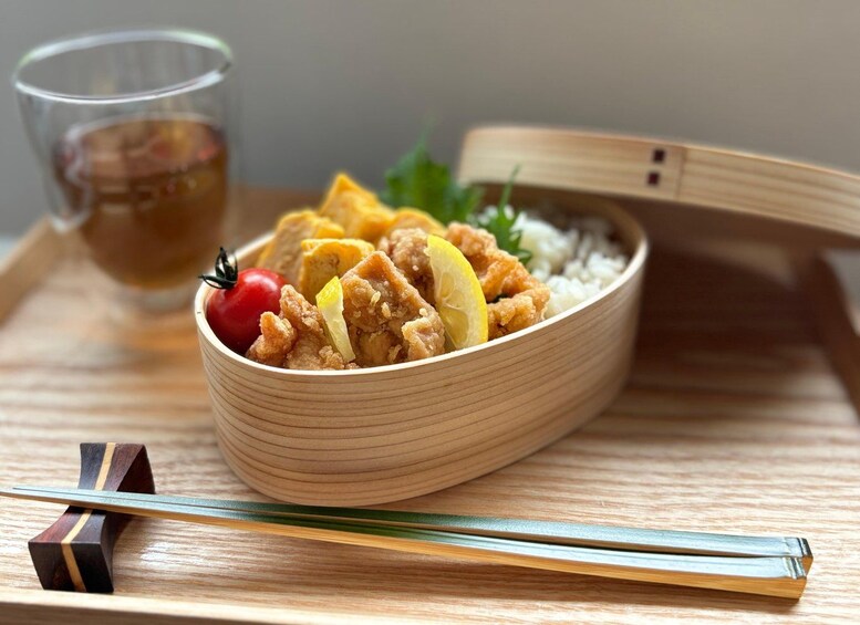 A bowl of fried chicken with lemon and tomato on a wooden tray. 1