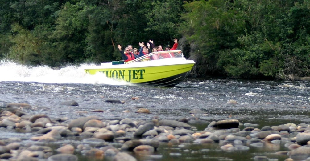 A yellow boat with 'LION JET' written on it, speeding across a river with people on board. 1