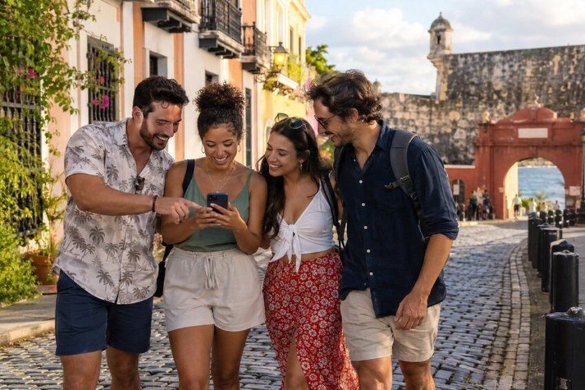 A group of people walking on a cobblestone street, with historic buildings and an archway in the background. 3