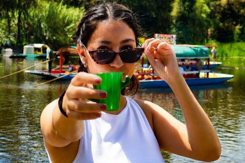 A person holding a green cup, with a boat and greenery in the background. 2
