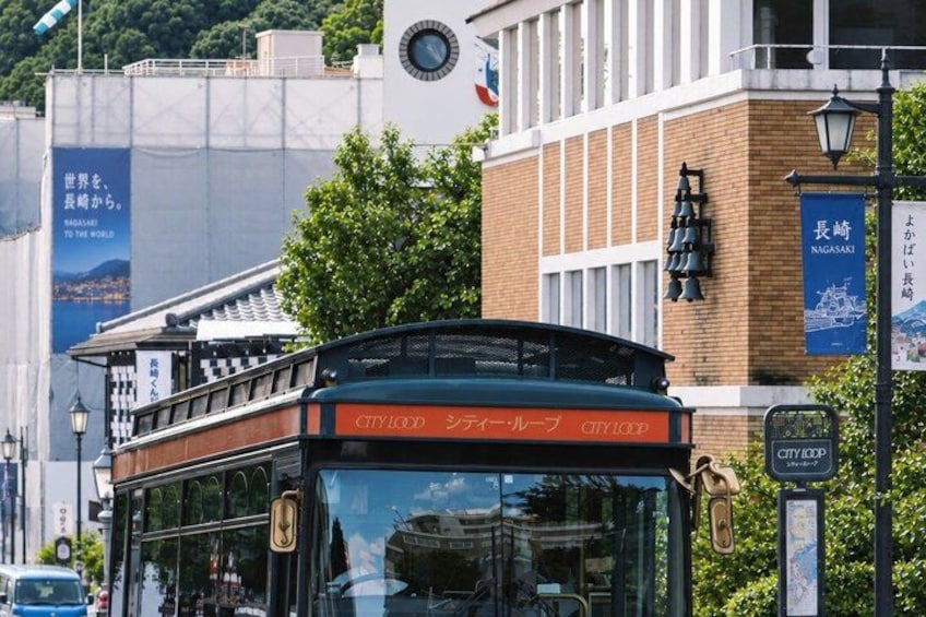 A city bus with 'CITY LOOP' written on it, a building with a clock, and a sign that says 'NAGASAKI'. 1