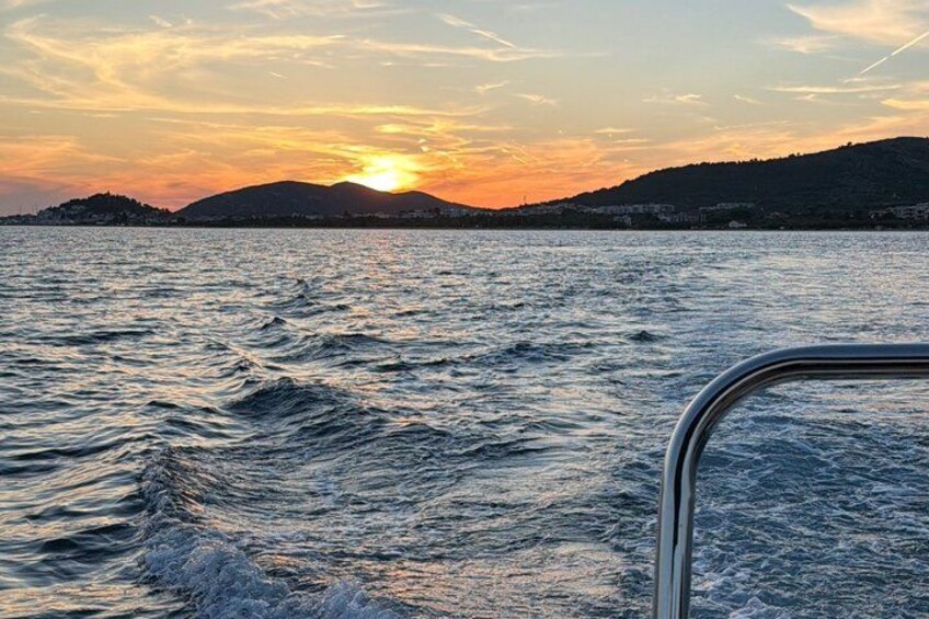 A sunset over a body of water with waves, a metal railing, and a distant shoreline with hills. 2