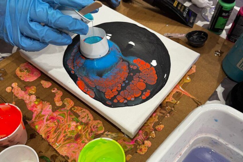 A person painting a circular object with blue and red paint on a white surface. 3