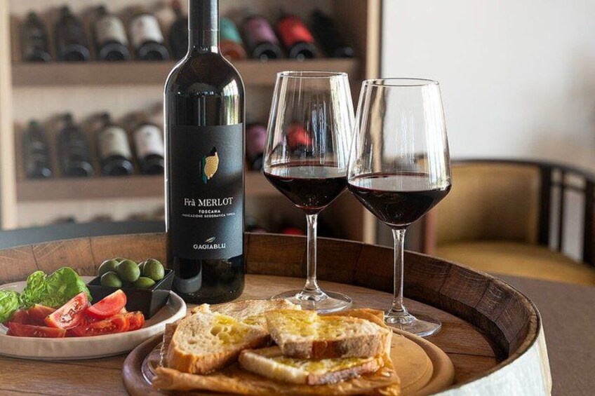 A bottle of Frà Merlot wine, two glasses of red wine, a plate with bread and vegetables, and a wooden tray. 1