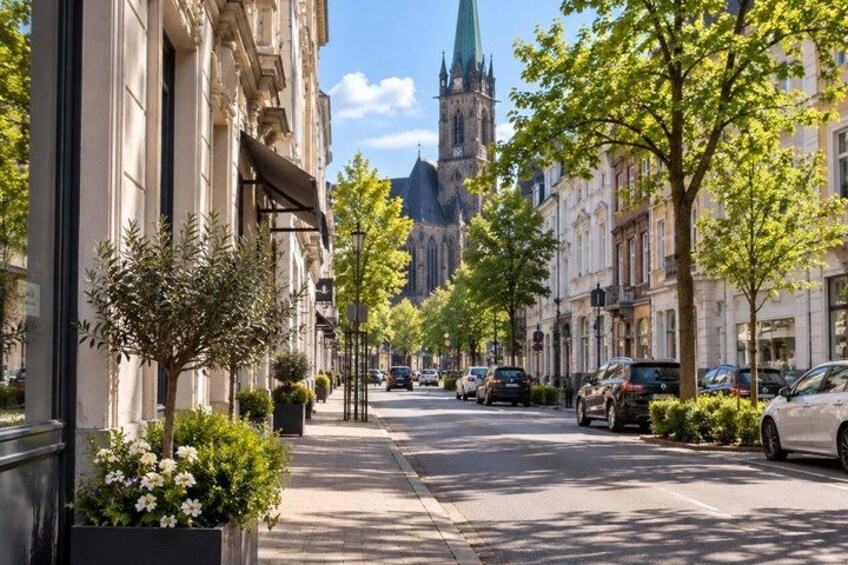A tree-lined street with parked cars and a church in the background. 2