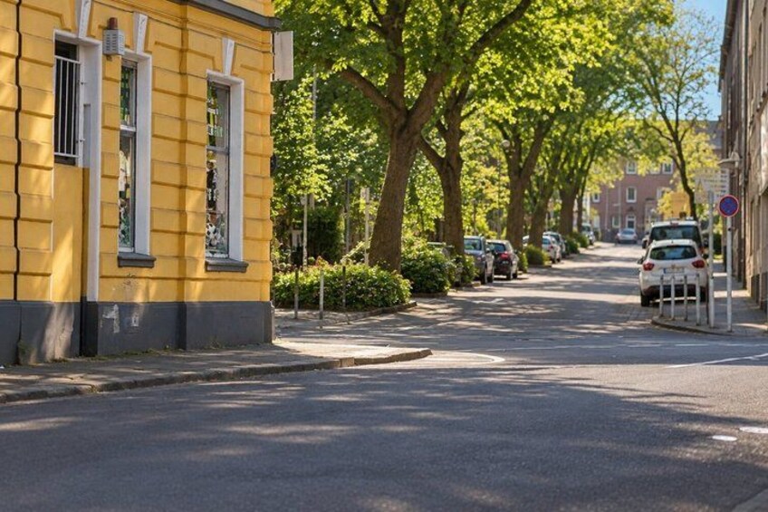 A yellow building with white trim, a tree-lined street, parked cars, and a no parking sign. 5
