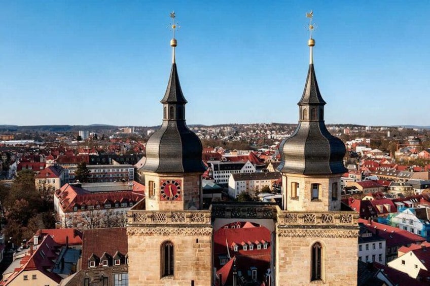 A town with two prominent towers, one with a clock, and a clear view of the surrounding buildings and landscape. 1