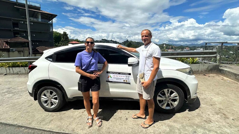 Two people standing next to a white car with a sign on the back. 4