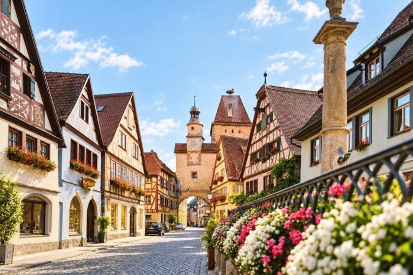 A cobblestone street lined with traditional half-timbered houses, a church tower, and blooming flowers. 3